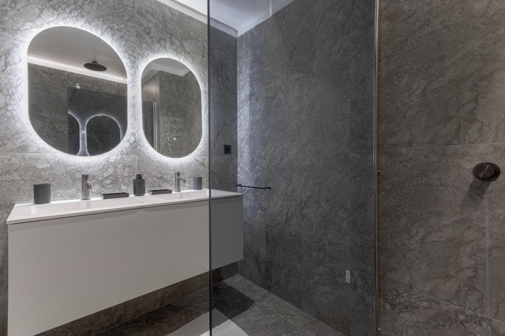 Salle de bain moderne en marbre gris, double vasque et miroirs ovales rétroéclairés.
